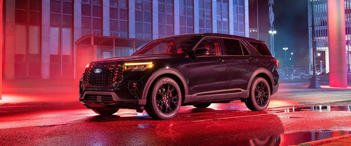 Black 2027 Ford Explorer with black wheels parked on a wet city street at night, lit by red light.